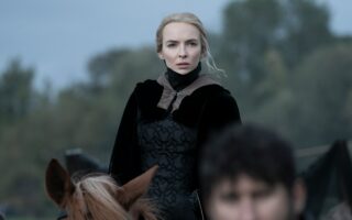 Jodie Comer als Maguerite de Carrouges in The Last Duel (2021): Eine blonde Frau sitzt in einem mittelalterlich inspirierten, schwarzen Kleid auf einem Pferd und sieht mit besorgtem Blick in Richtung der Kamera.
