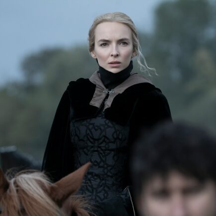 Jodie Comer als Maguerite de Carrouges in The Last Duel (2021): Eine blonde Frau sitzt in einem mittelalterlich inspirierten, schwarzen Kleid auf einem Pferd und sieht mit besorgtem Blick in Richtung der Kamera.