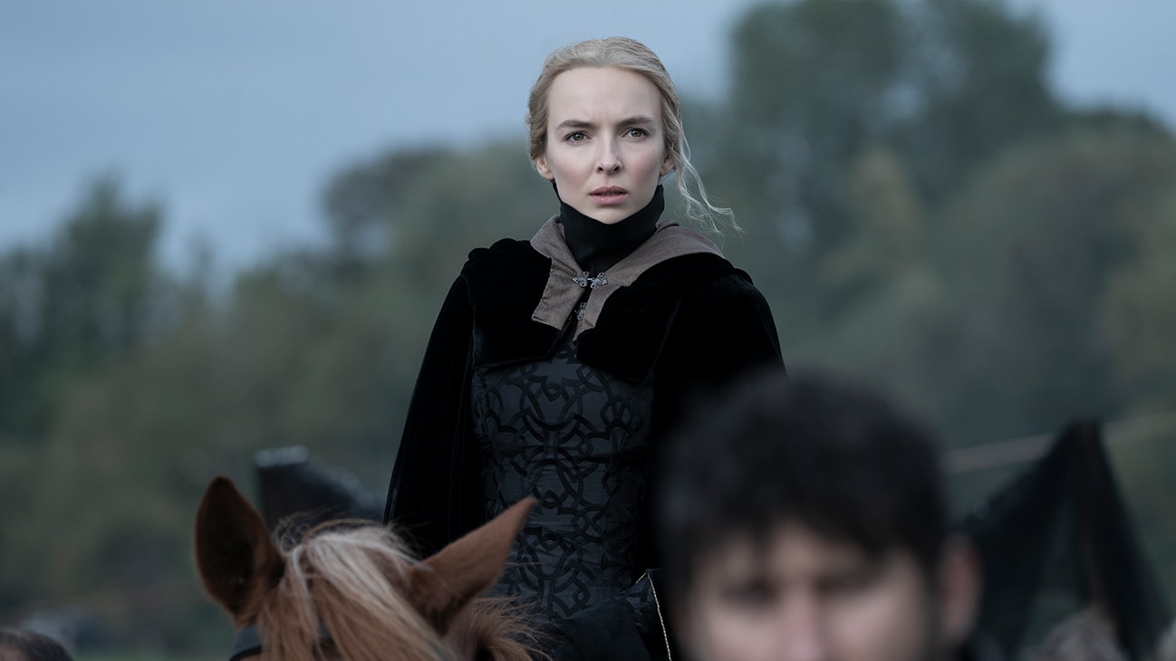 Jodie Comer als Maguerite de Carrouges in The Last Duel (2021): Eine blonde Frau sitzt in einem mittelalterlich inspirierten, schwarzen Kleid auf einem Pferd und sieht mit besorgtem Blick in Richtung der Kamera.